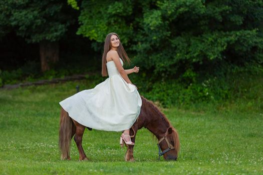 girl in a white dress rides a pony on a green lawn