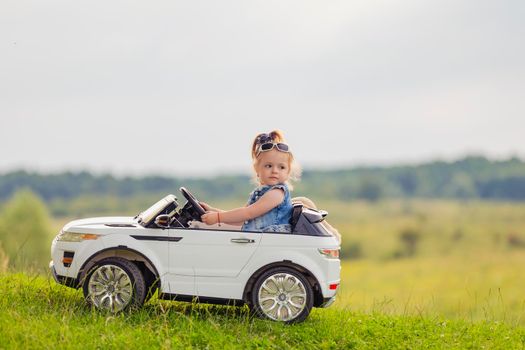 little girl rides on a children's car on a green lawn