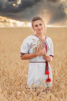 girl in the Ukrainian national costume on the background of a wheat field and sunset sun