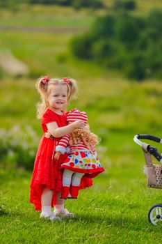 girl in a red dress and with a doll in her hands stands in nature