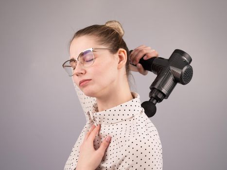 Caucasian business lady makes herself a back massage with a massager gun on a white background