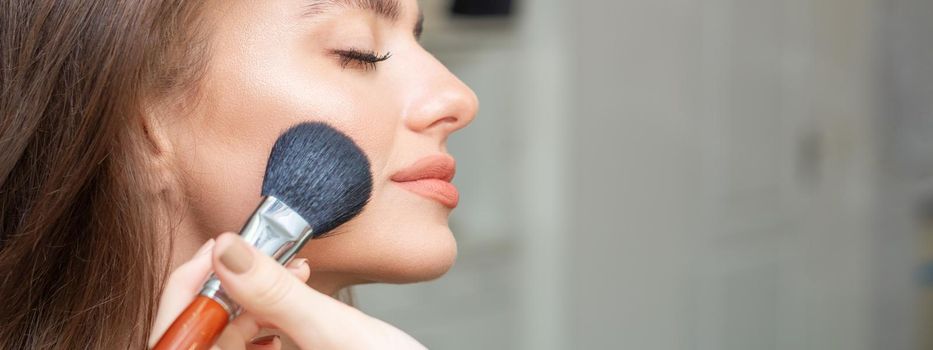 Make up artist applying professional make up of tonal foundation on the face of beautiful young caucasian woman in make up room. Base for make up.