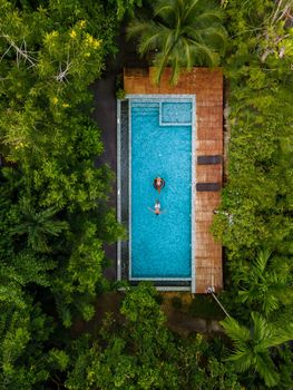 couple men and woman in swimming pool in the jungle of Krabi Thailand, aerial view with drone above swimming pool in jungle of Thailand.
