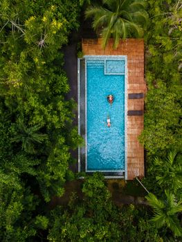 couple men and woman in swimming pool in the jungle of Krabi Thailand, aerial view with drone above swimming pool in jungle of Thailand.