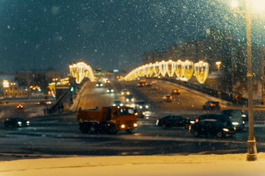 Falling snow on the background of cars with the headlights on at night in the center of Moscow. The concept of the first snow or snowfall in winter.