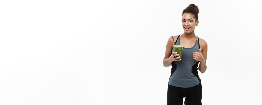 Healthy and Fitness concept - Beautiful American African lady in fitness clothing drinking healthy vegetable drink. Isolated on white background