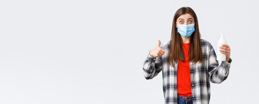 Coronavirus outbreak, leisure on quarantine, social distancing and emotions concept. Excited and satisfied girl in medical mask promote great hand sanitizer, preventing virus soap, thumb-up.