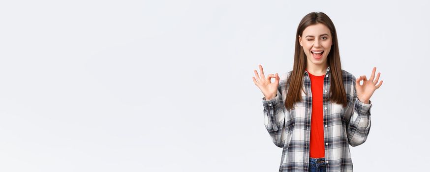 Lifestyle, different emotions, leisure activities concept. Confident and assured enthusiastic young woman in checked shirt assure all okay, promise or guarantee, show okay sign, smiling and wink.