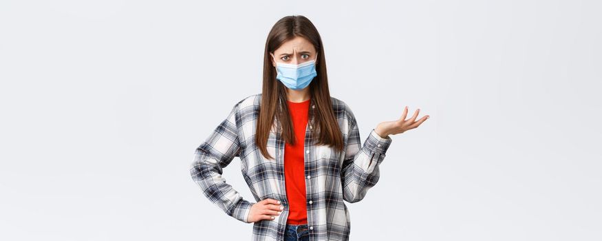 Coronavirus outbreak, leisure on quarantine, social distancing and emotions concept. Confused and bothered young woman cant understand this, shrug and stare puzzled camera, medical mask.