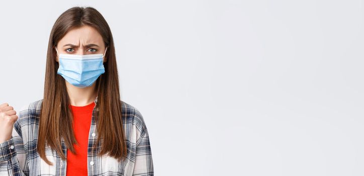 Coronavirus outbreak, leisure on quarantine, social distancing and emotions concept. Upset and disappointed young woman in medical mask frowning, condemn smth, pointing finger left displeased.