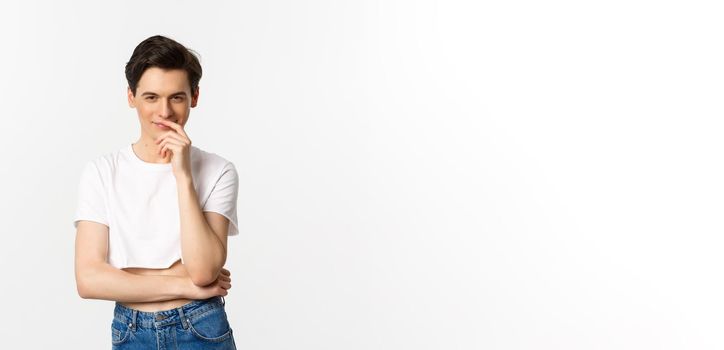Lgbtq and pride concept. Satisfied young gay man thinking, having an idea and smiling while staring at camera, wearing crop top, white background.