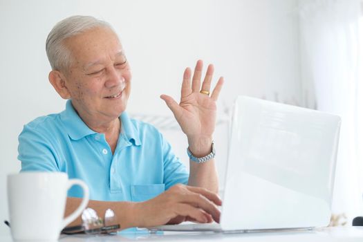 Elderly man making video call and waving at screen, chatting with children, communication with friend distantly, older generation modern tech easy comfortable usage concept..