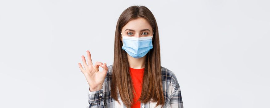 Coronavirus outbreak, leisure on quarantine, social distancing and emotions concept. Close-up of satisfied good-looking woman in medical mask, assure all good, show okay guarantee gesture.
