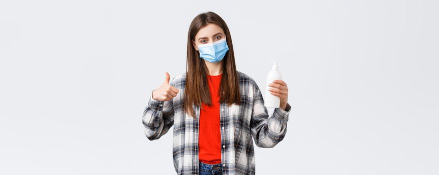 Coronavirus outbreak, leisure on quarantine, social distancing and emotions concept. Satisfied female customer, shop client in medical mask advice this hand soap or hand sanitizer, thumb-up.