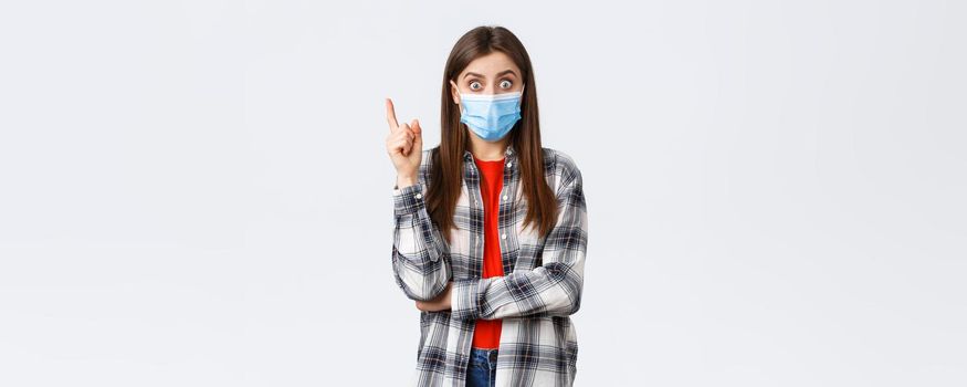 Coronavirus outbreak, leisure on quarantine, social distancing and emotions concept. Excited smart young woman in medical mask and checked shirt, raising index finger to say suggestion, have idea.