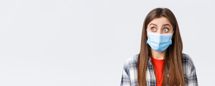 Coronavirus outbreak, leisure on quarantine, social distancing and emotions concept. Close-up of surprised caucasian woman in casual clothes and medical mask, staring left speechless.