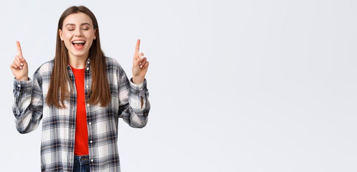 Lifestyle, different emotions, leisure activities concept. Dreamy and happy pretty young woman in checked shirt, dream came true, showing summer vacation resort, pointing fingers up with closed eyes.