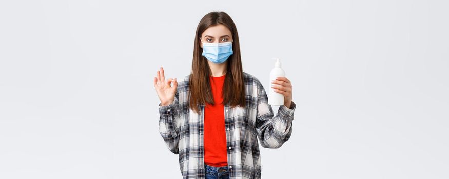 Coronavirus outbreak, leisure on quarantine, social distancing and emotions concept. Self-assured young woman in medical mask recommend hand soap or sanitizer, show okay sign.