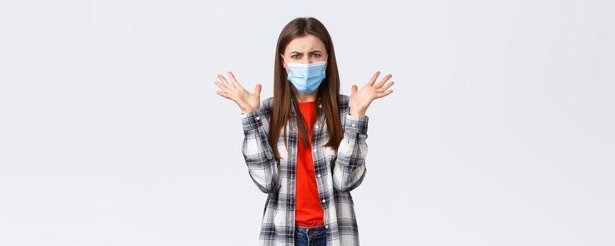 Different emotions, covid-19 pandemic, coronavirus self-quarantine and social distancing concept. Angry, outraged woman in medical mask, arguing, look mad, raise hands in dismay, complaining.