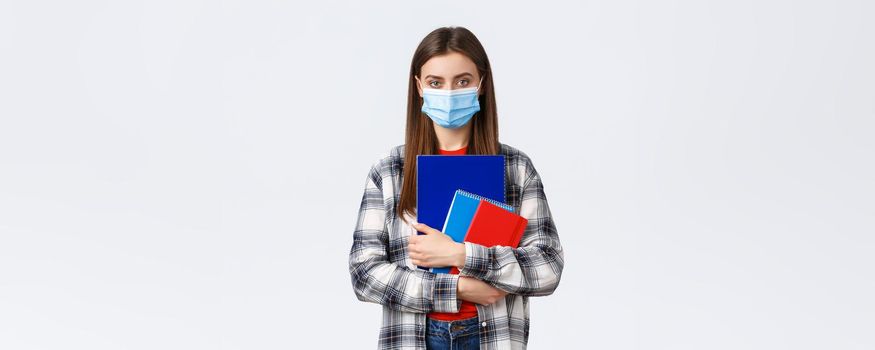 Coronavirus pandemic, covid-19 education, and back to school concept. Young female student in medical mask holding notebooks, going to class, freshman in university in personal protective facemask.