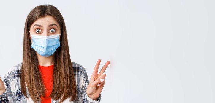 Coronavirus outbreak, leisure on quarantine, social distancing and emotions concept. Close-up of excited and thrilled cute woman in medical mask, showing peace sign or quotes, stare impressed.
