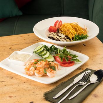 A dinner table with meals with hummus, shrimp, vegetables and beef