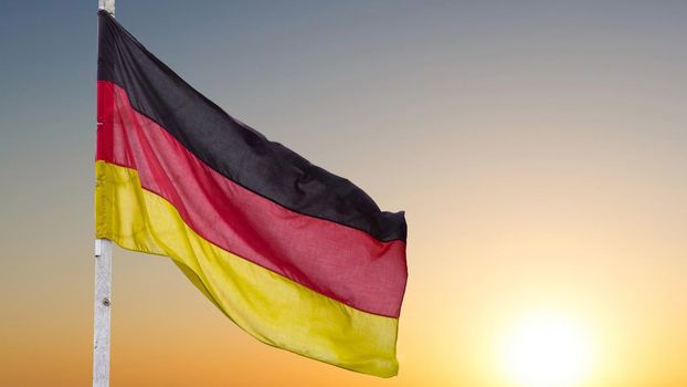 The official flag of Germany waving on a blue sky background. Horizontal banner design, with the German flag hanging on a sunny background with white clouds. Deutschland flag wide banner.