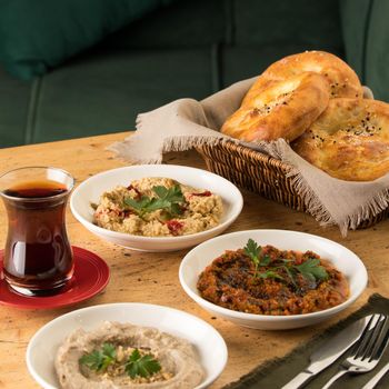 A photo of Mediterranean dishes, baba ganoush, muhammara and hummus with a basket of bread