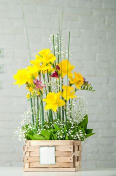 A vertical shot of a beautiful composition with daffodils and pink freesia in a wooden box