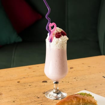A healthy strawberry smoothie in a mug with drinking tubules next to baklava on a wooden table