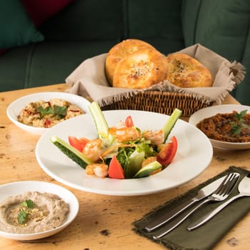 A dining table full of delicious salad on a white plate next to basket of bread