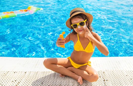 The child is putting sunscreen on her face. Selective focus. Kid.