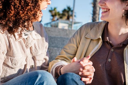 detail of a couple of lesbian women laughing holding hands, concept of sexual freedom and racial diversity