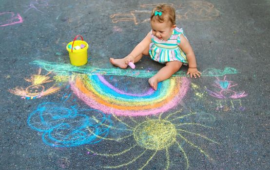 Baby draws a rainbow on the pavement with chalk. Selective focus. Nature.