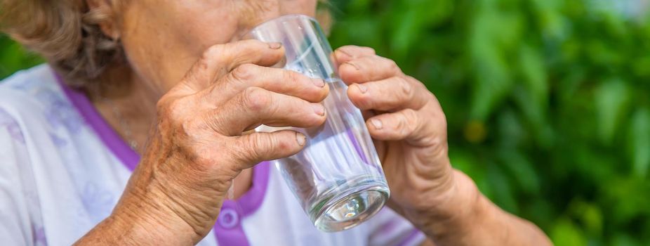 Grandma drinks water from a glass. Selective focus. Woman.