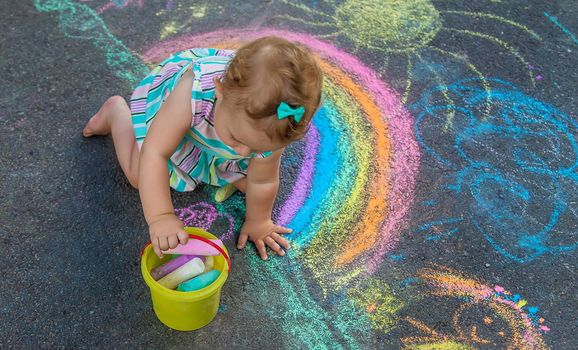 Baby draws a rainbow on the pavement with chalk. Selective focus. Nature.