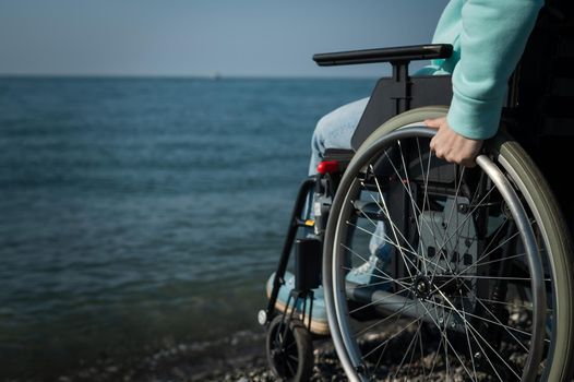 Caucasian woman in a wheelchair on the seashore. Close-up of female hands