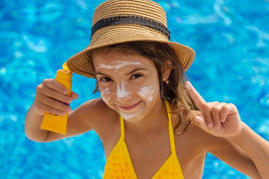 The child is putting sunscreen on her face. Selective focus. Kid.