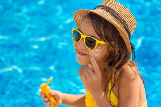 The child is putting sunscreen on her face. Selective focus. Kid.