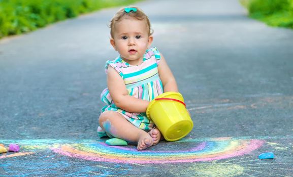 Baby draws a rainbow on the pavement with chalk. Selective focus. Nature.