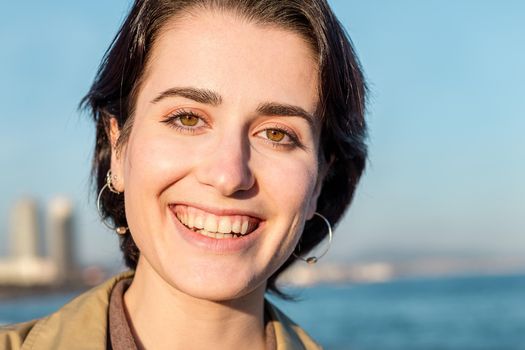portrait of a young lovely girl with short hair and beautiful green eyes smiling in front of a blue sky background, concept of beauty, youth and diversity, copy space for text
