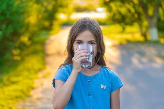 The child drinks water from a glass. Selective focus. Kid.