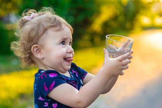 The child drinks water from a glass. Selective focus. Kid.