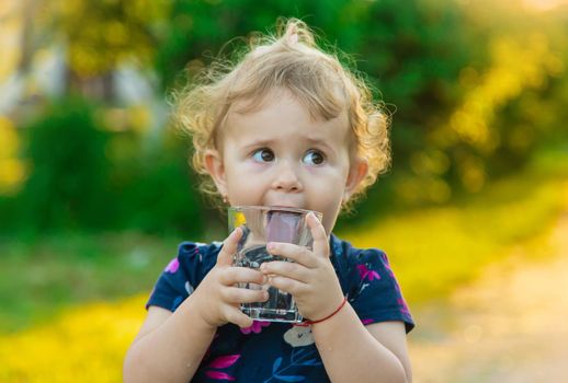 The child drinks water from a glass. Selective focus. Kid.