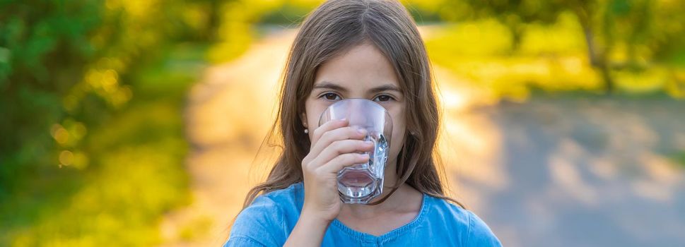 The child drinks water from a glass. Selective focus. Kid.