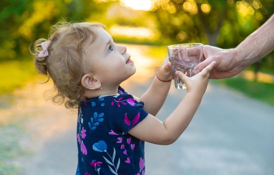 The child drinks water from a glass. Selective focus. Kid.