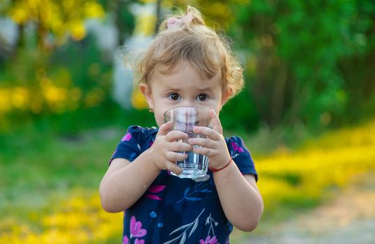 The child drinks water from a glass. Selective focus. Kid.