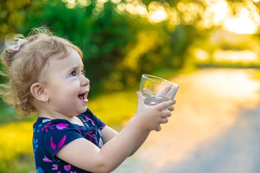 The child drinks water from a glass. Selective focus. Kid.