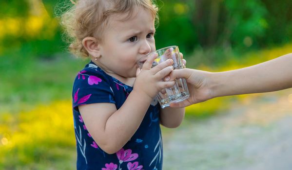 The child drinks water from a glass. Selective focus. Kid.