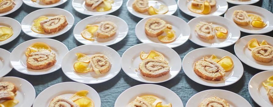Sponge rolls with jam and a slice of orange on white plates. background. Banner.